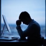 Young office professional sitting with poor posture and experiencing neck and back pain while working on a laptop.