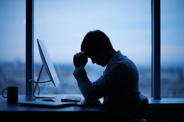 Young office professional sitting with poor posture and experiencing neck and back pain while working on a laptop.