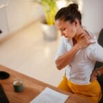 Young office professional suffering from neck and back pain due to prolonged sitting and poor posture at work